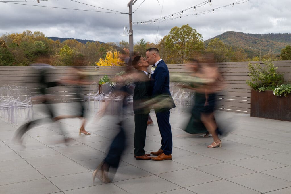 grooms kissing while bridal party run past