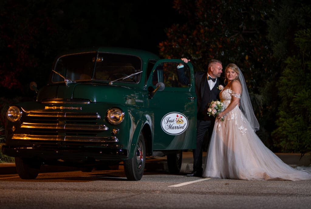 Wedding couple posing at night beside a vintage green truck with a just married sign on the driver's side door